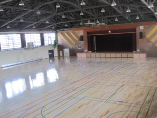 前方に舞台があり、端にバスケットゴールが設置されている多目的ホールの写真