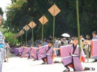 ピンク色の衣装を着た人々が立膝をして立傘（たてがさ）を持っている七川祭りの様子の写真