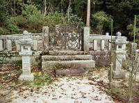 後方を山々に囲まれ、コンクリートで覆われた墓地に近藤重蔵の墓が建っている写真