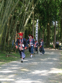 頭に陣笠をかぶり紺かすりの着物を着て、 桐の木の馬頭に竹をさした竹馬にまたがっている人々の写真