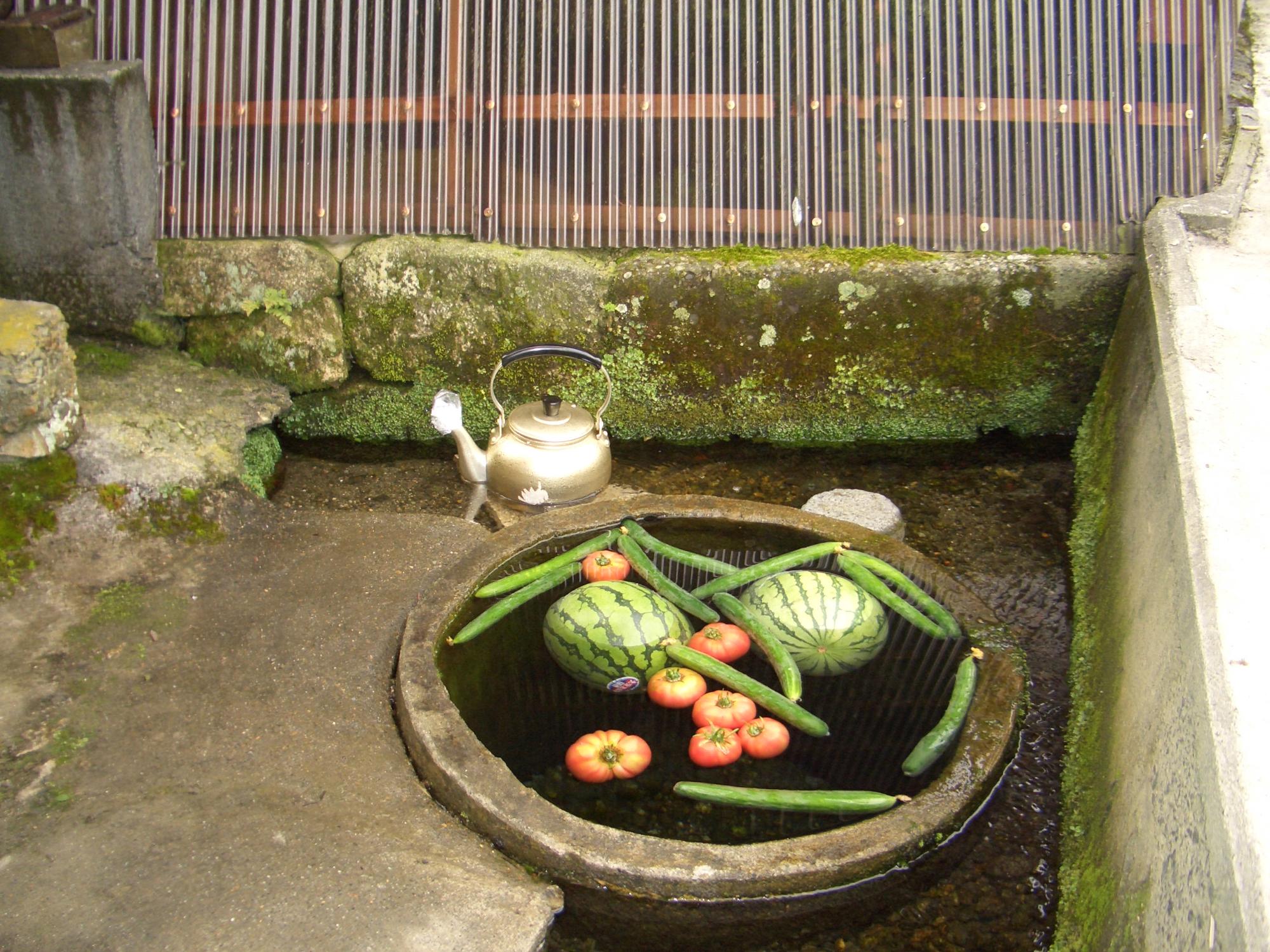 コンクリートで出来たカバタ（洗い場）にスイカやキュウリ、トマトを浮かべている写真