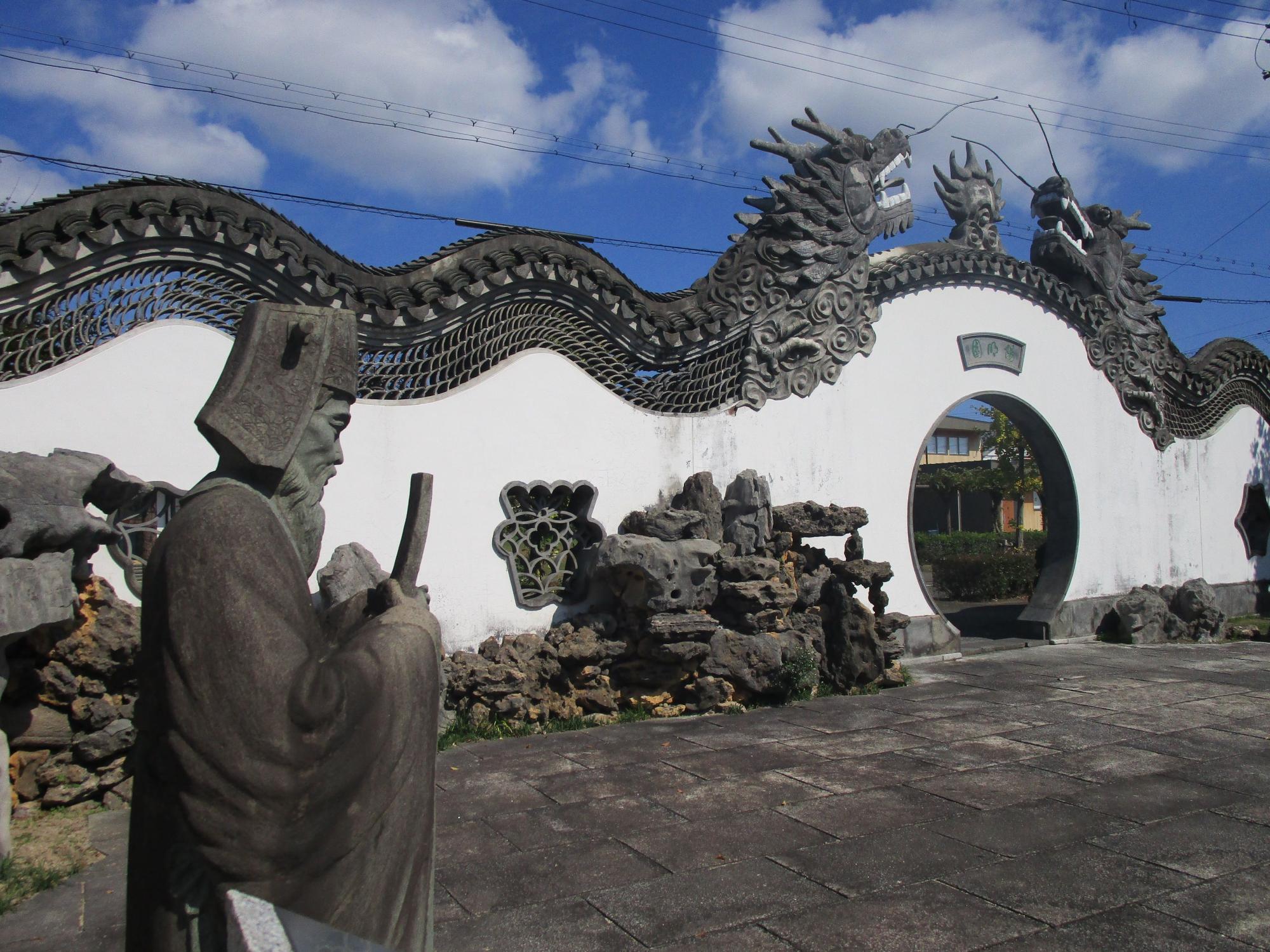 手前に王陽明の像が建ち、丸い形をした入り口と、巨大な龍瓦が乗っている陽明園入り口を左側から写した写真