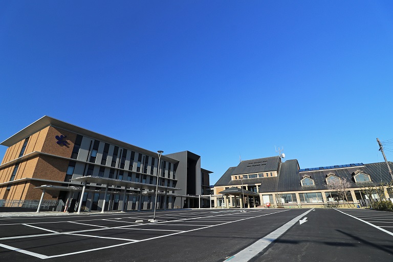 広い駐車場の奥に、左側に新館・右側に本館が見える高島市役所本庁舎の外観写真