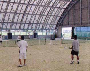 屋根付き多目的グラウンド内のテニスコートでテニスをしている利用者の写真