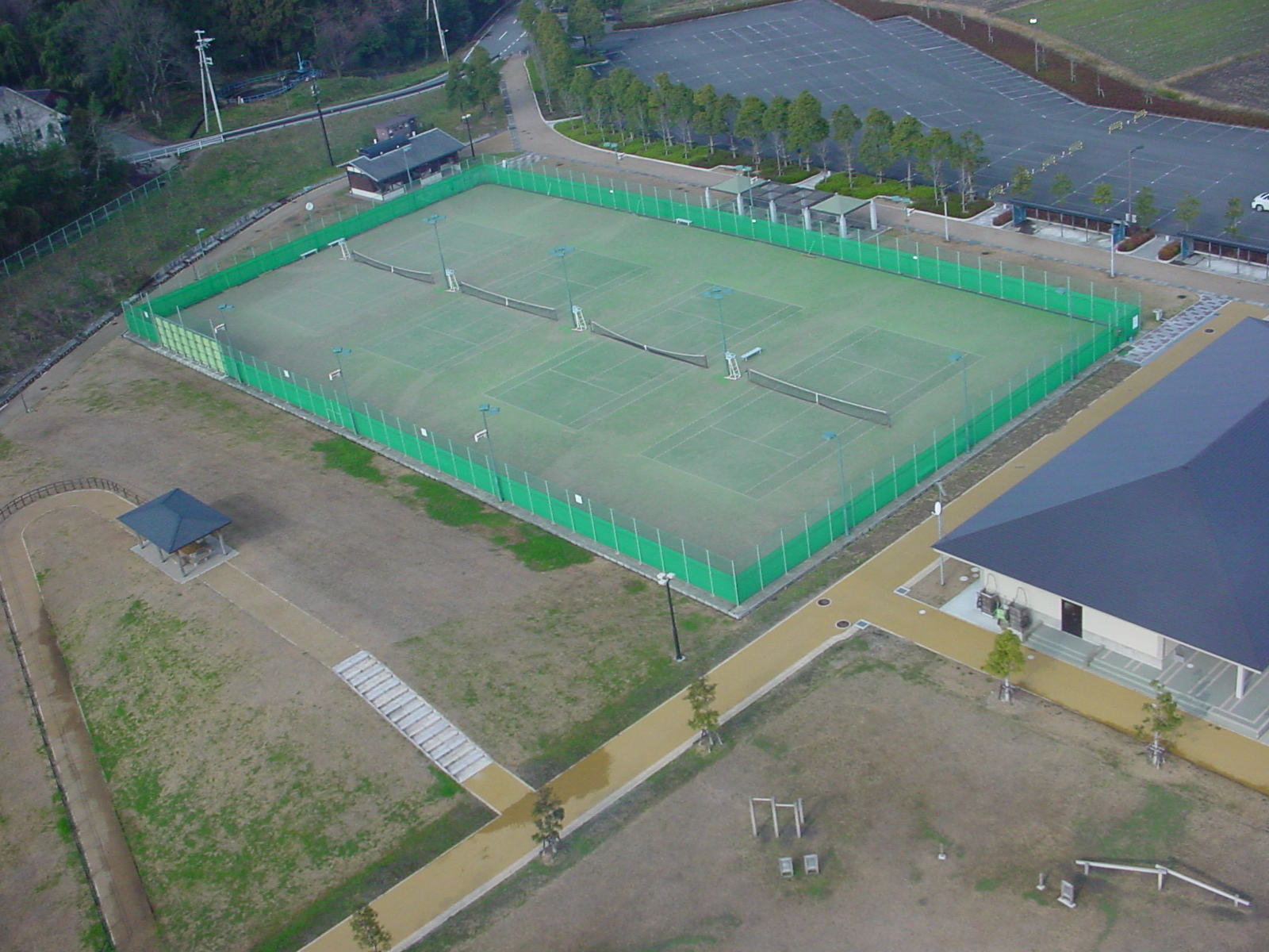 緑色のフェンスで囲まれたテニスコートを上空から撮影した写真