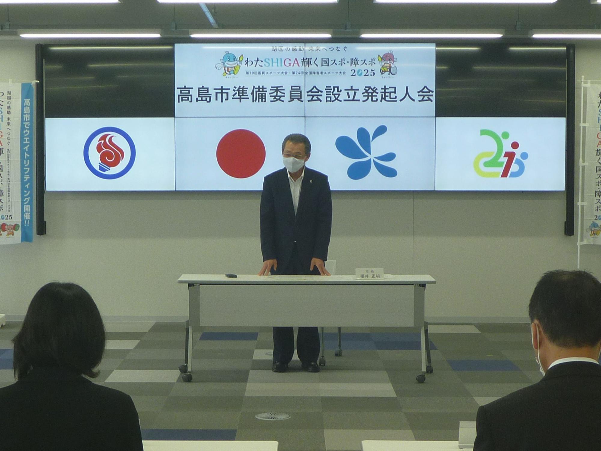 「高島市準備委員会設立発起人会」と書かれたボードの前に立ち話をしている福井市長の写真